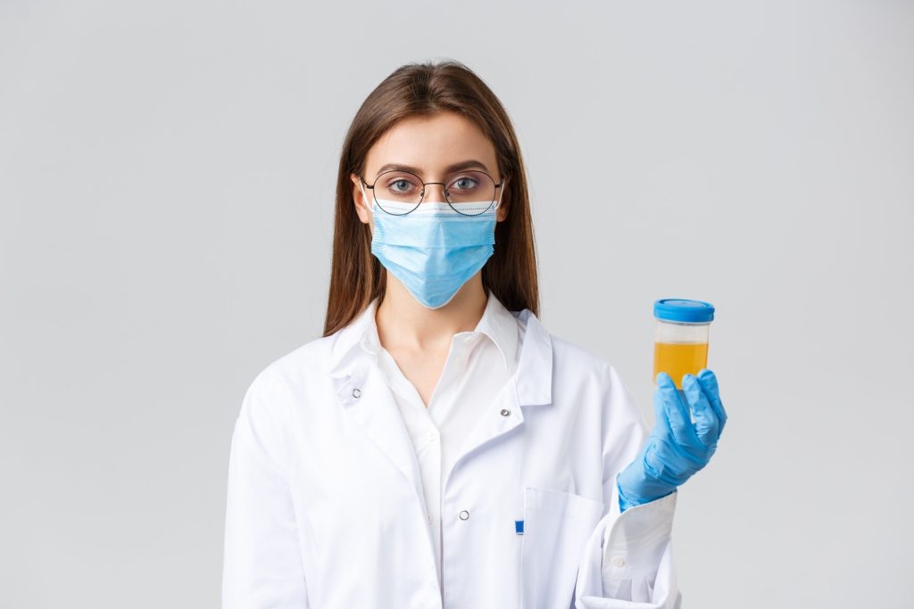 A doctor in a lab coat holding a urine sample for an affordable DOT physical in Houston, wearing gloves and a mask.