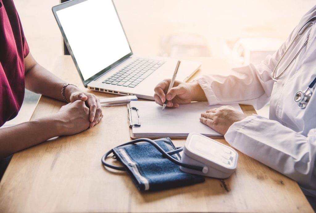 Doctor documents patient info beside blood pressure monitor during Best Price DOT Physical Houston evaluation.