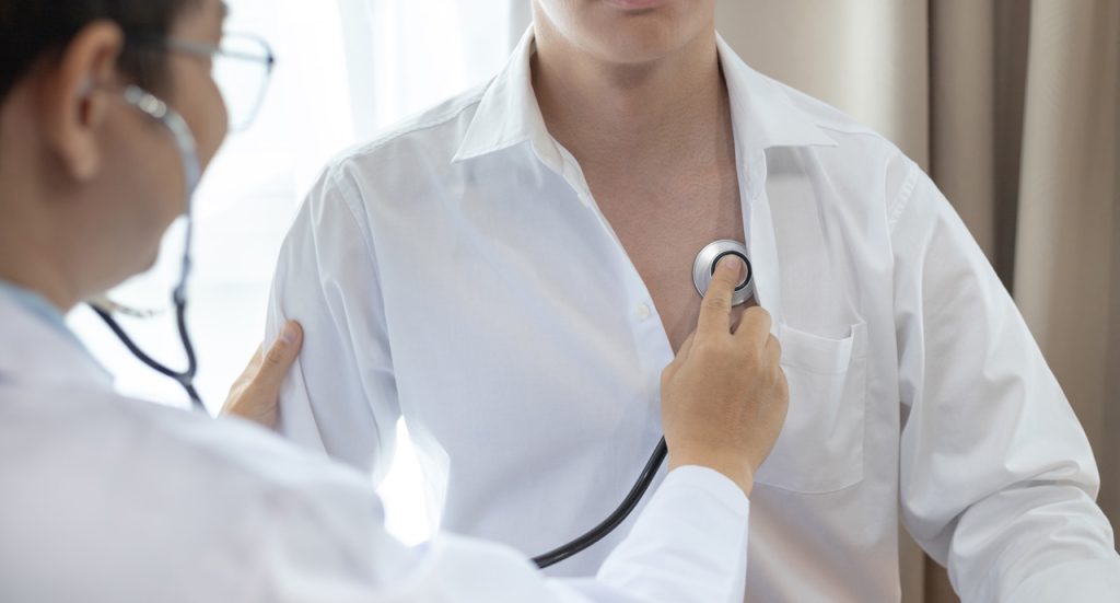 A DOT certified medical examiner Houston performing a heart check with a stethoscope during a driver physical.