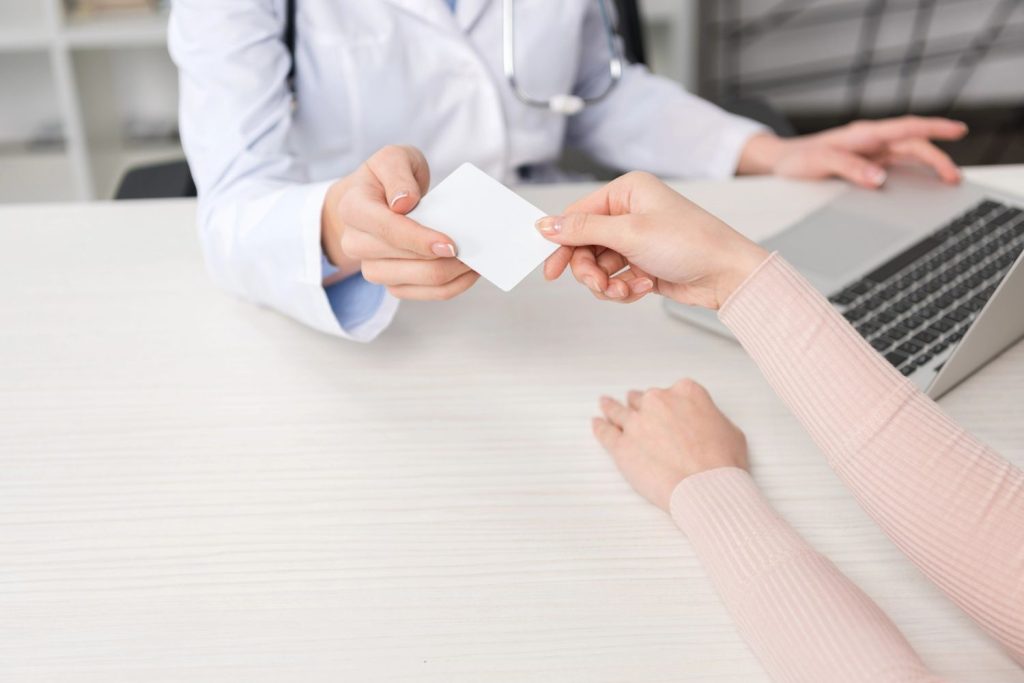 A medical examiner at a laptop handing a CDL medical card in Houston to a driver during an appointment. 