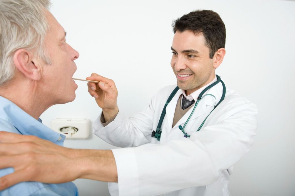 Close up of a doctor using a penlight and tongue depressor for a CDL medical card Houston DOT physical exam.
