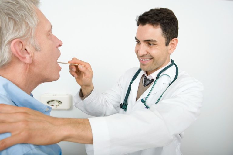 Close up of a doctor using a penlight and tongue depressor for a CDL medical card Houston DOT physical exam.