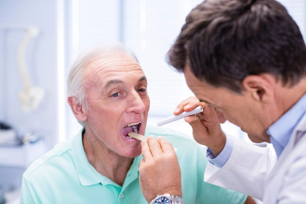 A smiling doctor uses a tongue depressor to examine a patient for their CDL medical card Houston physical exam. 