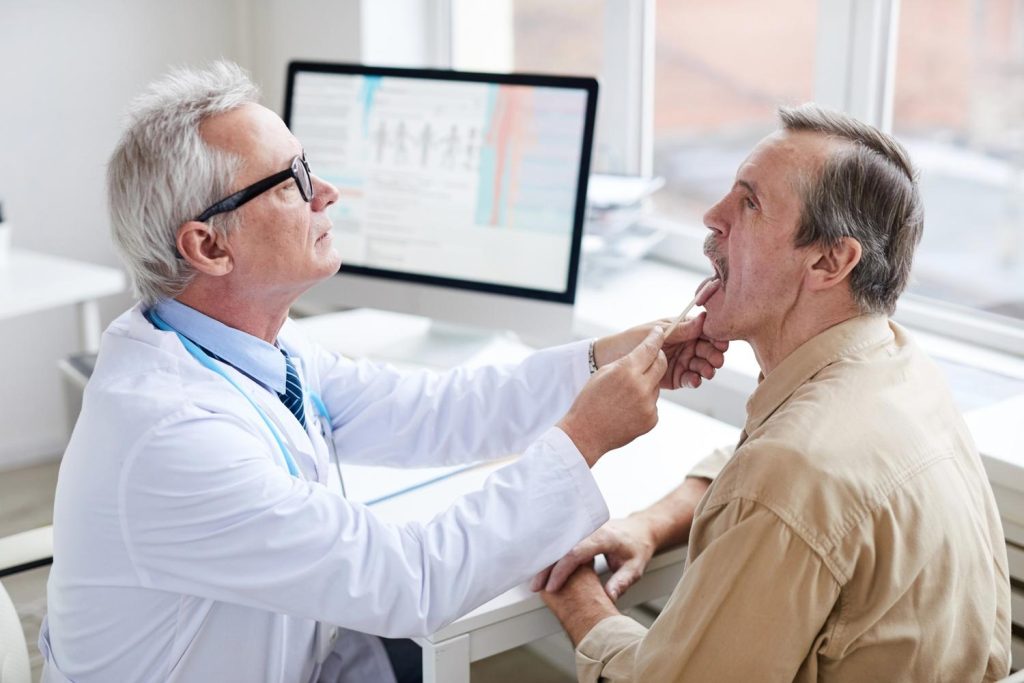 Male doctor performing a throat examination on a driver as part of a required DOT physical Houston TX checkup. 