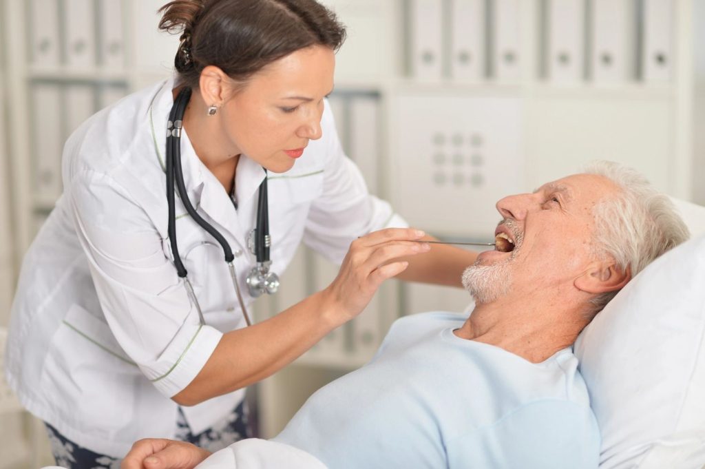 A female doctor performs a throat exam for a senior man during a CDL medical card Houston certification checkup. 
