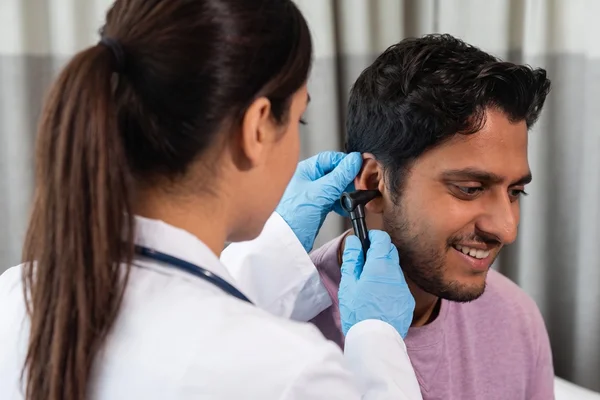 Female doctor checking a patient's ear with an otoscope for a DOT medical exam.